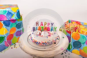 Decorated Birthday cake happy birthday candles on cake stand wrapped gifts on solid background