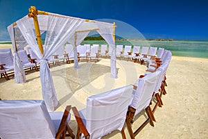 Decorated chairs and arch for wedding ceremony on tropical island with sandy beach and tourquise clear water. photo