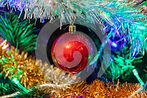 Decorated Christmas tree closeup shot. Red ball in the middle, illuminated garland with blue, orange, green lights. New Years,