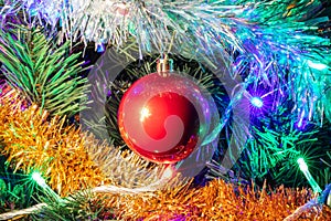 Decorated Christmas tree closeup shot. Red ball in the middle, illuminated garland with blue, orange, green lights. White and