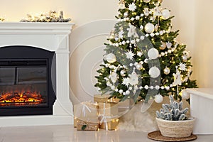 Decorated Christmas tree with faux fur skirt and gift boxes near fireplace indoors