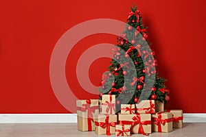 Decorated Christmas tree and gift boxes near red wall