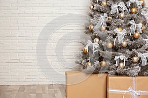 Decorated Christmas tree and gift boxes near brick wall, closeup. Space for text