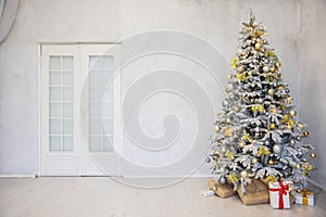 Decorated Christmas tree with gifts in white room interior