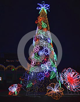 Decorated Christmas tree outside with lights covered with bright toys. Decorated streets and buildings