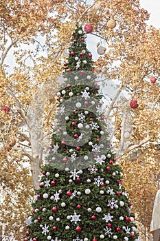 Decorated Christmas tree outside. Tree decorated with red, white and silver ball ornaments, white snowflake ornaments and small