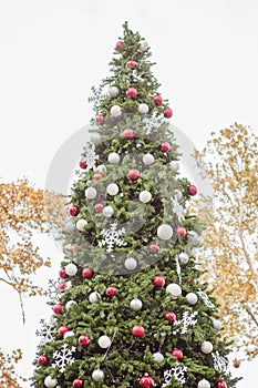 Decorated Christmas tree outside. Tree decorated with red, white and silver ball ornaments, white snowflake ornaments and small