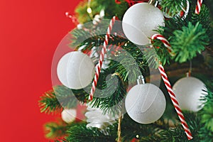 Decorated Christmas tree with white and red seasonal tree ornaments like baubles and candy canes on red background