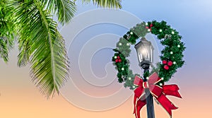Decorated Christmas wreath around an illuminated street lamp post on a tropical destination.