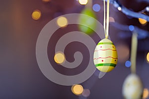 Decorated colorful Easter egg hanging on tree branch indoor with warm bokeh on background