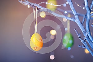 Decorated colorful Easter egg hanging on tree branch indoor with warm bokeh on background