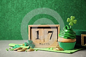 Decorated cupcake, wooden calendar, hat and coins on grey table. St. Patrick`s Day celebration