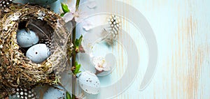 Decorated Easter eggs in nest and spring flower on table background