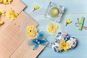 Decorated Easter eggs, yellow flowers, burning candle on wooden blue boards background. Spring and Easter concept.