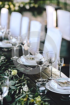 Decorated elegant wooden wedding table in rustic style with eucalyptus and flowers, porcelain plates and glasses