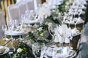 Decorated elegant wooden wedding table in rustic style with eucalyptus and flowers, porcelain plates and glasses