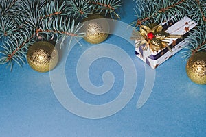 Decorated gift box on blue background, surrounded by christmas golden balls and pine branches