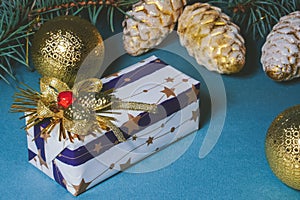 Decorated gift box on blue background, surrounded by christmas toys balls and pine branches and cones