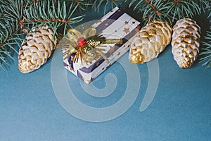 Decorated gift box on blue background, surrounded by christmas toys balls and pine branches and cones