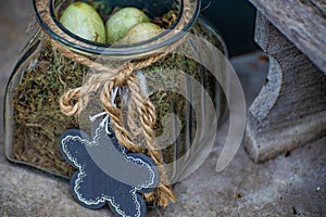 Decorated glass with three green little bird eggs on green dry moss. Blackboard on a cord as flower shape for text