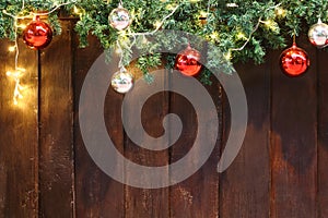 Decorated green Christmas tree branch by colorful red and silver bauble ball and yellow light on top of aged brown wood wall