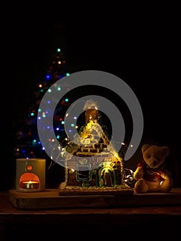 Decorated homemade sweet gingerbread house soft bear, glowing candle in aroma lamp diffuser, festive garland decorations