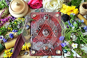 Decorated magic book, quill, summer herbs and flowers on witch table