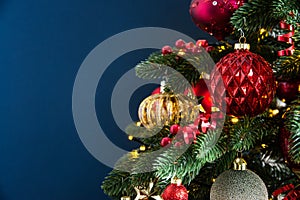 Decorated with ornaments and lights Christmas tree on dark blue background. Merry Christmas and Happy Holidays greeting card