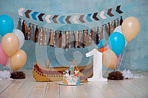 Decorated photo zone for 1 year Indian Apache chief with a canoe for a children`s party. First birthday and smash cake