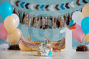 Decorated photo zone for 1 year Indian Apache chief with a canoe for a children`s party. First birthday and smash cake