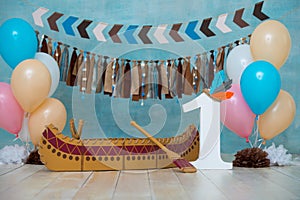Decorated photo zone for 1 year Indian Apache chief with a canoe for a children`s party. First birthday and smash cake