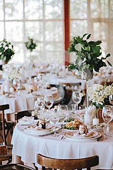 A decorated rustic wedding table with a white tablecloth of porcelain plates with glasses, decorated with flowers with