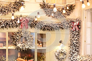 Decorated street window with garland spruce branches and Xmas wreath with red bow. Winter welcome wreath, decorating building.