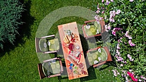 Decorated table with cheese, strawberry and fruits in beautiful summer rose garden, aerial top view of table food and drinks
