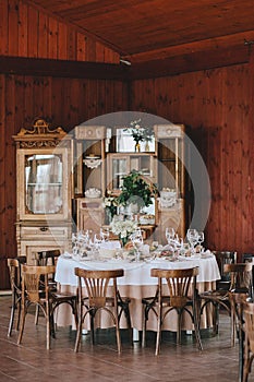 Decorated wedding table in rustic style for dinner with white and beige tablecloths, wine glasses with flowers and