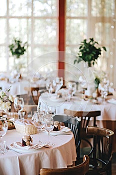 Decorated wedding table in rustic style for dinner with white and beige tablecloths, wine glasses for flowers and