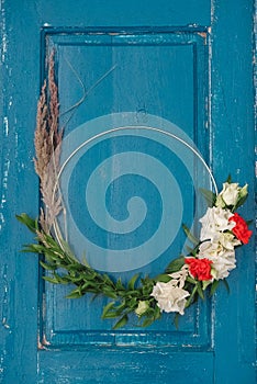 Decorated wreath of flowers, leaves and dry grass on a wooden blue door background. Copy, empty space for text