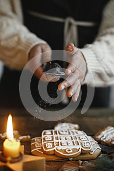 Decorating christmas gingerbread cookies with sugar powder on rustic wooden table with candle and ornaments. Christmas holiday