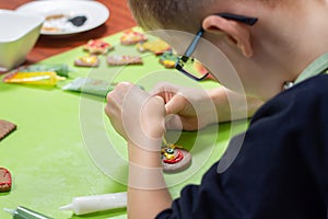 Decorating cinnamon cookies by a child. The boy`s hands form a face of colored icing squeezed out of tubes. Unaddressed biscuits i