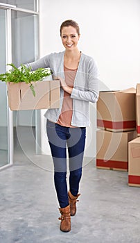 Decorating her new office. A young businesswoman carrying a box into her new office.