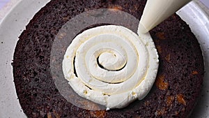 Decorating home baked chocolate cake. Female hands piping out whipped cream on a sponge cake.