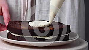 Decorating home baked chocolate cake. Female hands piping out whipped cream on a sponge cake.