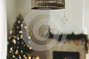 Decorating home with christmas straw spiders. Rustic nordic straw decoration hanging on background of festive golden lights bokeh