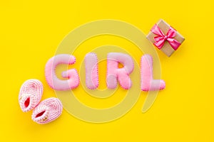 Decoration for baby`s birthday. Word girl near booties and present box on yellow background top view