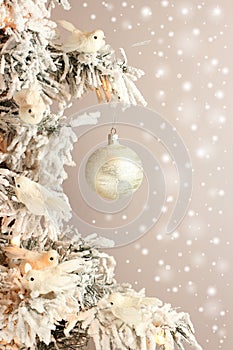 Decoration on Christmas tree - white birds and silver ball on snowy spruce on light gray background with snow mist