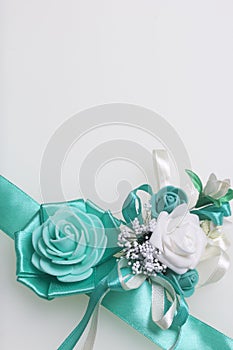 Decoration on hand in the form of a rose of emerald color, sewn to a satin ribbon. Near the wedding boutonniere. On a white backgr