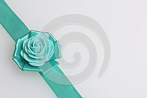 Decoration on hand in the form of a rose of emerald color, sewn to a satin ribbon. On a white background.