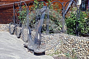 Decoration from an old black iron anchor on a chain on the street on a gray sidewalk near a stone fence