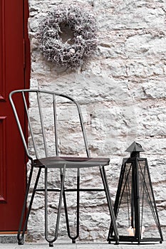 Decorations with metal chair, wreath and candle sconce. Home exterior. Front door decor. Red door with silver wreath