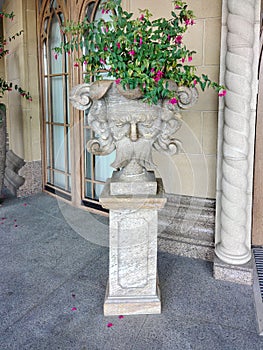 Decorative antique stone vase with flowers in the form of a head near the wall